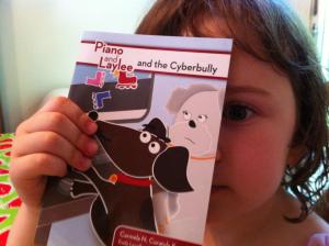 4 year old girl holding "Piano and Laylee and the Cyberbully" over her eye