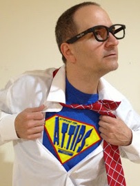 A picture for Chris wearing black-framed glasses pulling open a white shirt to reveal a super hero logo resembling the A.T.TIPSCAST log on it